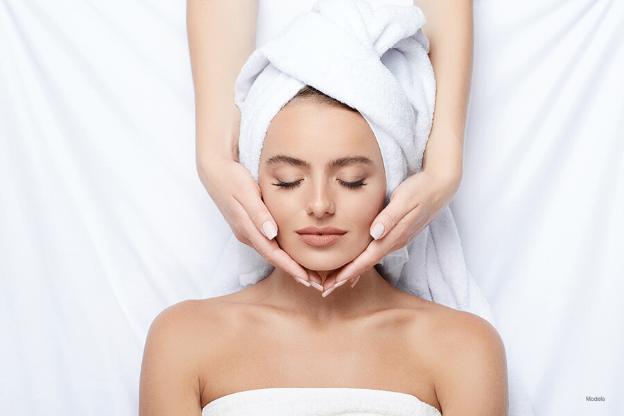 woman laying down with a towel on her head, getting her face massaged by someone else.