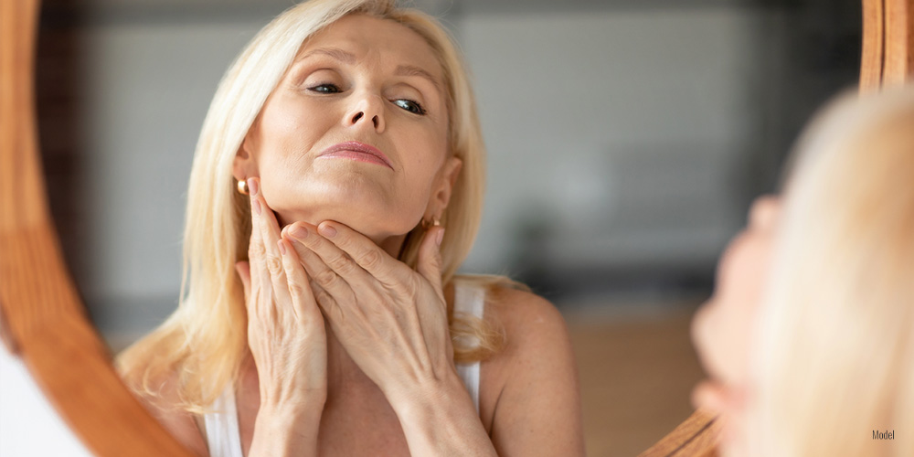 Woman looking in a mirror and touching her neck.